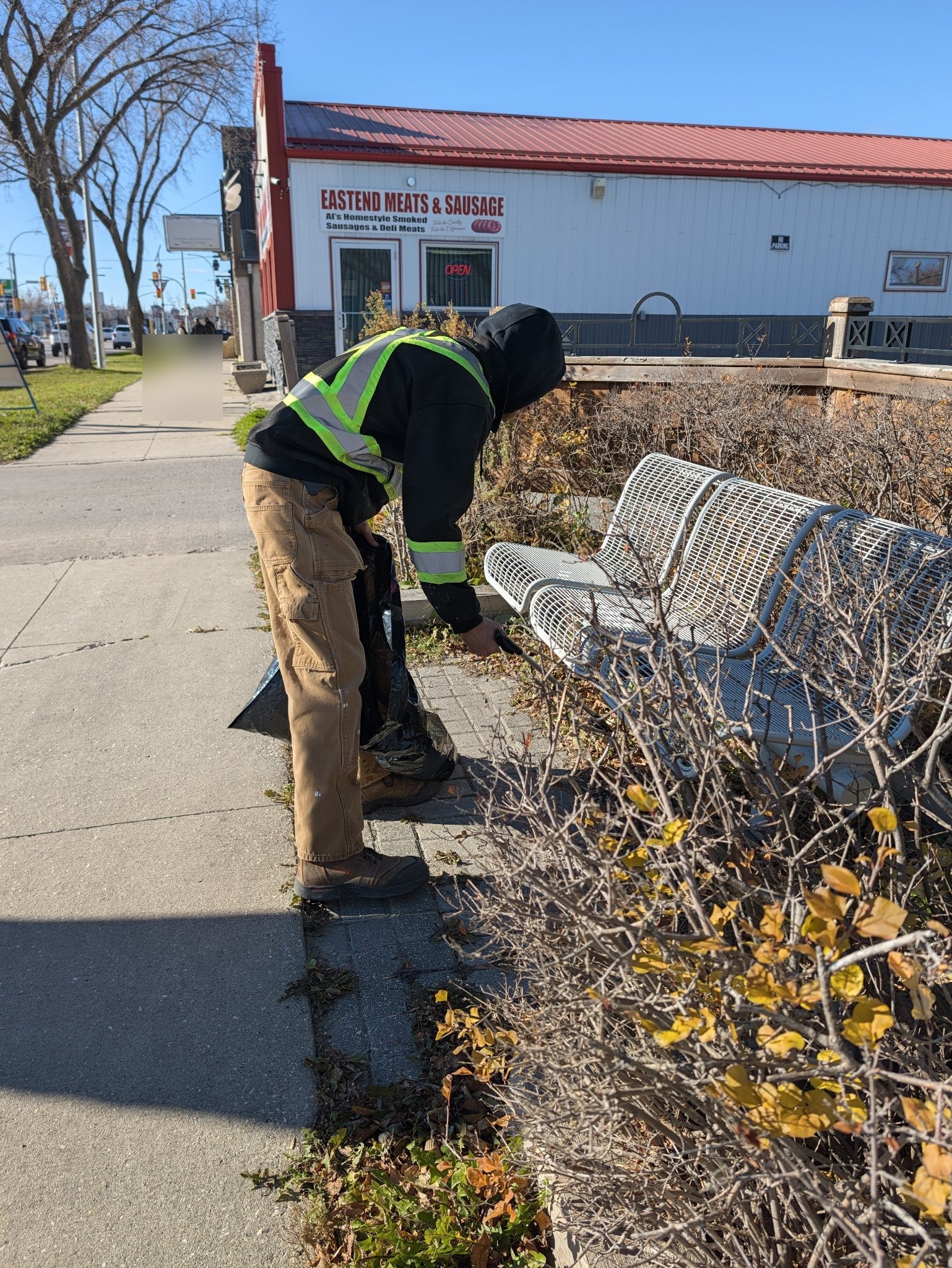 Nicholas picking up trash by benches near Eastend Meats in Transcona